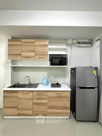 Modern kitchen with wooden cabinets, stainless steel fridge, and microwave in a compact layout.