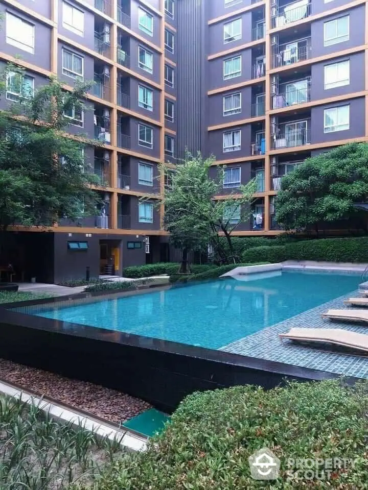 Luxurious residential complex with a serene pool area surrounded by lush greenery and modern apartment facades, offering a tranquil urban retreat.