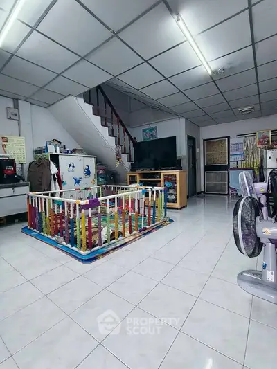 Spacious living room with playpen, TV, and staircase in family-friendly home.