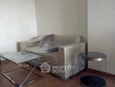 Modern living room with sleek furniture and plastic-wrapped sofa, showcasing minimalist design.