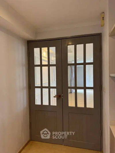 Elegant double doors leading to a spacious living area with wooden flooring.