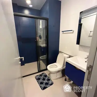 Modern bathroom with a sleek glass shower enclosure, bold blue vanity, and white fixtures, offering a clean and contemporary look.