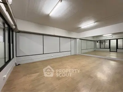 Spacious room with wooden flooring and large mirrors, ideal for dance or fitness studio.