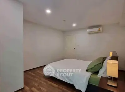 Cozy bedroom with modern decor and wooden flooring, featuring a comfortable bed and ambient lighting.