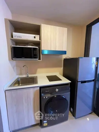 Modern compact kitchen with washing machine, microwave, and fridge in a sleek apartment.