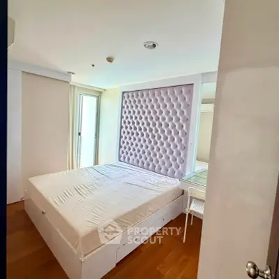 Spacious bedroom with modern design and ample natural light, featuring a stylish padded headboard and wooden flooring.