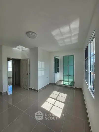 Spacious sunlit room with tiled flooring and large windows in modern apartment