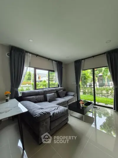 Spacious living room with large windows and garden view, featuring a modern gray sectional sofa and sleek coffee table.