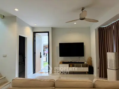Modern living room with sleek TV setup and stylish ceiling fan, inviting natural light through open door.