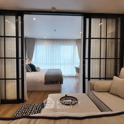 Luxurious modern living room with glass doors leading to a cozy bedroom, featuring elegant decor and ample natural light.