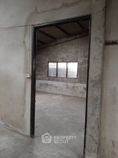 Spacious industrial-style room with concrete walls and large windows.
