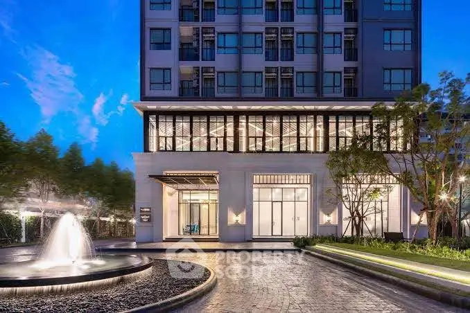 Elegant building exterior with fountain and landscaped entrance at dusk.