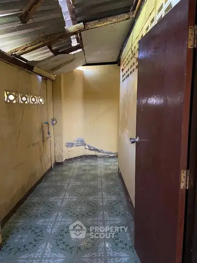 Rustic hallway with vintage tiles and exposed ceiling in need of renovation.