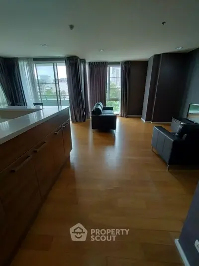 Spacious modern living room with wooden flooring and large windows offering city views.