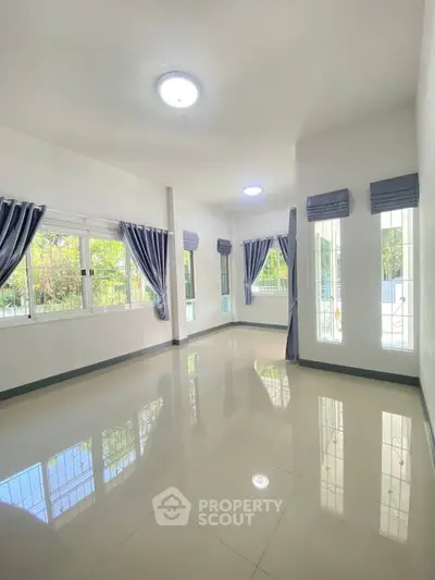 Spacious sunlit living room with large windows and elegant curtains