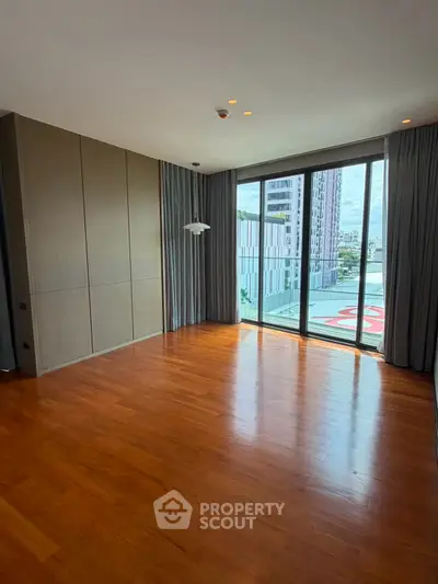 Spacious empty room with wooden flooring and large windows offering city views, perfect for customization.