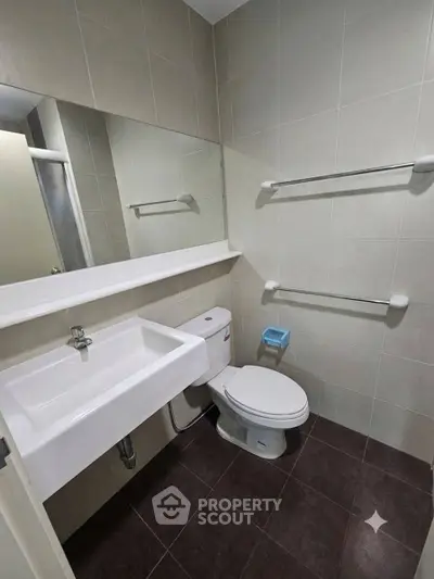 Modern bathroom with sleek fixtures and neutral tiles, featuring a spacious mirror and contemporary design.