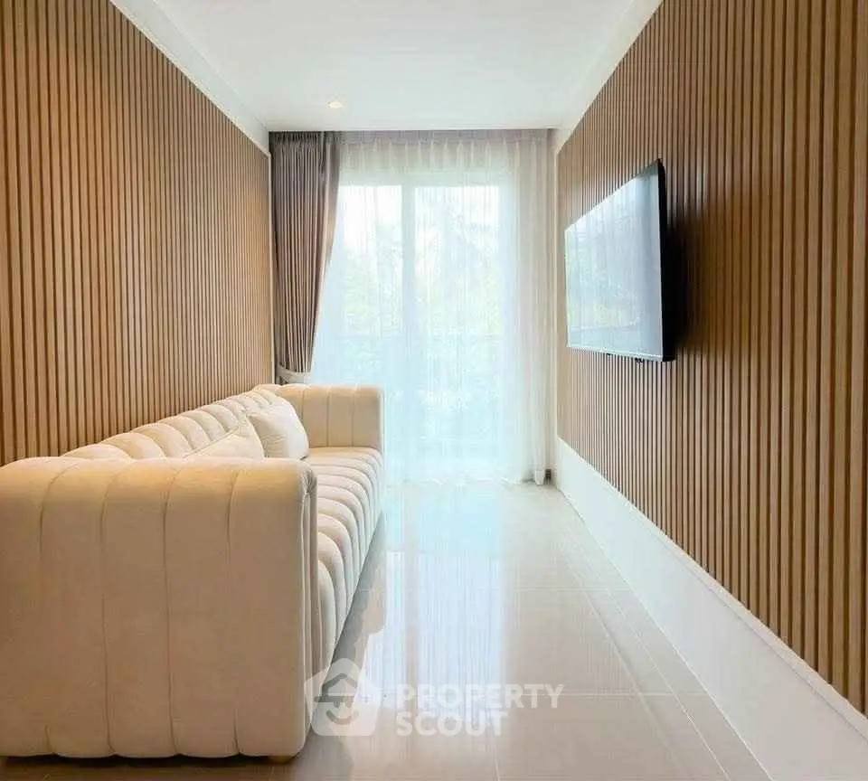 Modern living room with elegant white sofa and wall-mounted TV, featuring stylish wood paneling and large window.