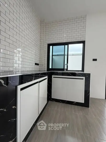 Modern kitchen with sleek black and white design, featuring tiled walls and large window.