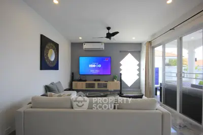 Modern living room with large sofa, wall-mounted TV, and sliding glass doors to balcony.