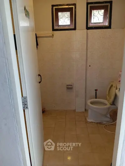 Cozy bathroom with tiled walls and small windows, featuring a classic toilet design.