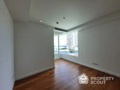 Spacious and bright corner unit with large windows offering a panoramic city view, featuring polished hardwood floors and a modern, airy ambiance.