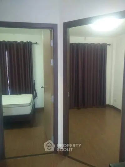 Cozy apartment with two bedrooms featuring wooden flooring and dark curtains.