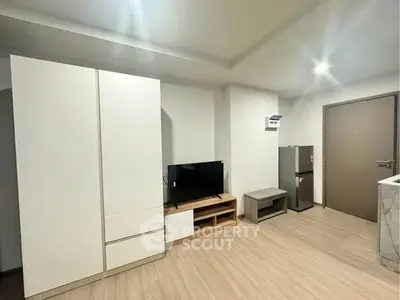 Modern living room with sleek furniture and minimalist design, featuring a TV and compact refrigerator.