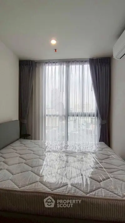 Spacious bedroom with large window and modern decor in high-rise apartment.