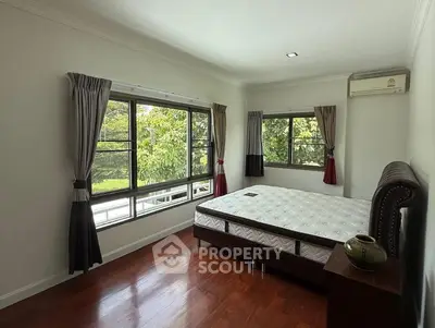 Spacious bedroom with large windows and wooden flooring, featuring a comfortable bed and lush green views.