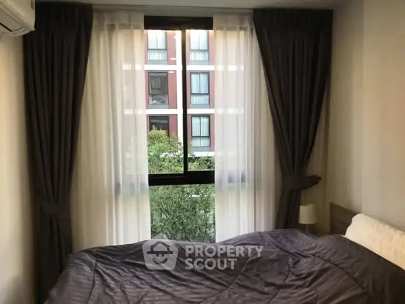 Cozy bedroom with large window and elegant curtains overlooking greenery.