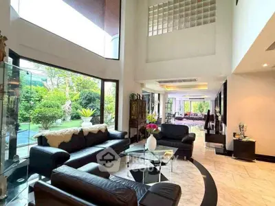 Luxurious living room with high ceilings and garden view, featuring elegant black leather sofas and modern decor.