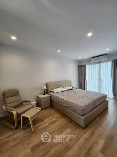 Spacious bedroom with modern decor and natural light, featuring a comfortable bed and stylish armchair.