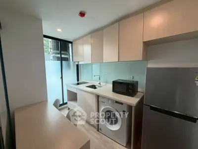 Modern kitchen with sleek cabinetry, washing machine, and microwave in a compact layout.