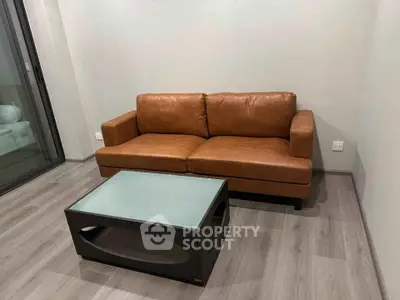 Modern living room with brown leather sofa and sleek glass coffee table on wooden flooring.