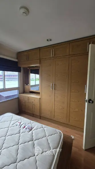 Spacious bedroom with built-in wooden wardrobe and large window view.