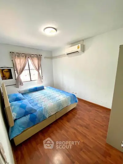 Cozy bedroom with wooden flooring and air conditioning, featuring a large bed and natural light.