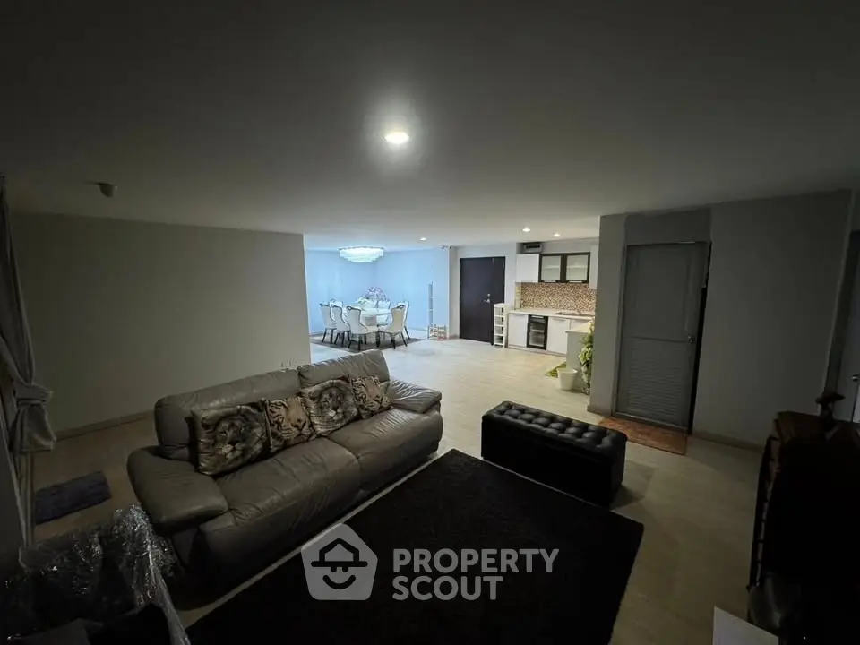 Spacious open-plan living room with modern kitchen and dining area, featuring elegant lighting and cozy seating.