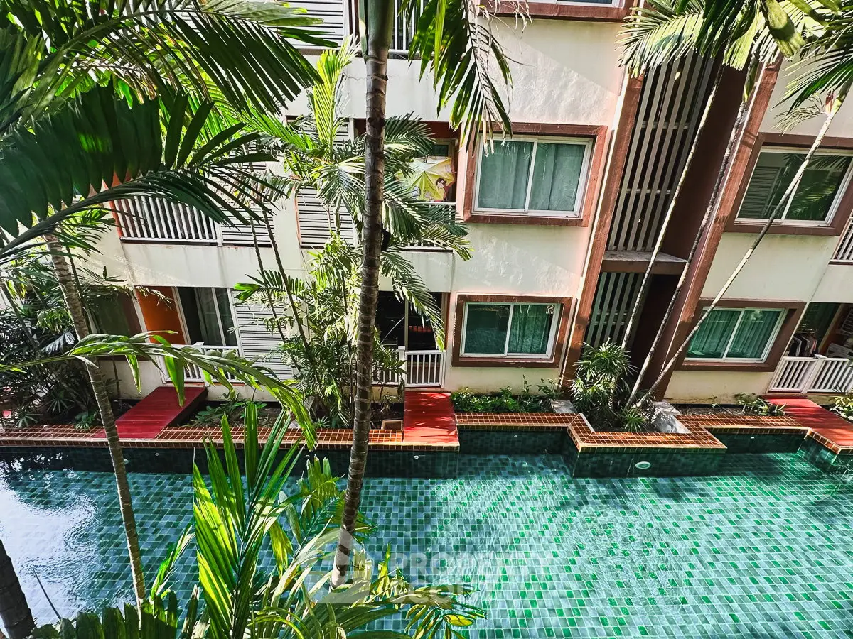 Luxurious apartment building with a stunning pool surrounded by lush greenery, offering a serene tropical retreat.