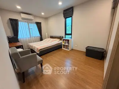Spacious bedroom with wooden flooring, cozy bed, and ample natural light from large windows.