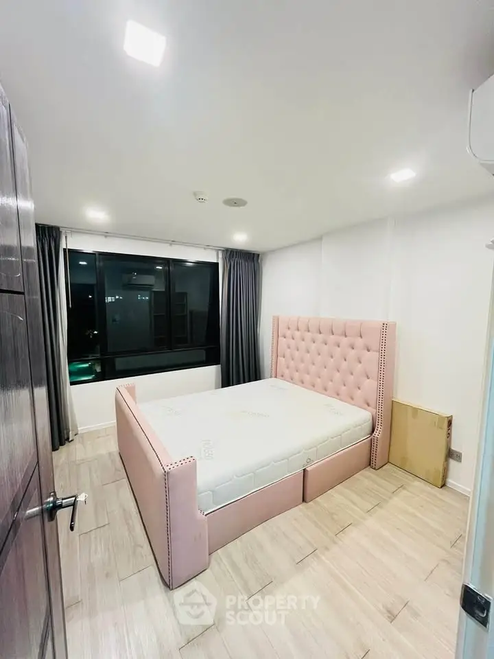 Modern bedroom with stylish pink bed and large window offering city views.