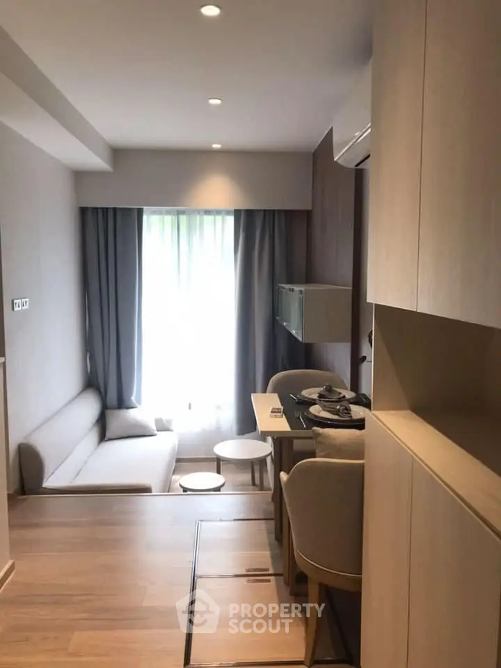 Modern studio apartment with integrated living and kitchen space, featuring sleek cabinetry, comfortable seating, and natural light filtering through sheer curtains.