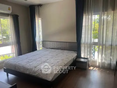 Spacious bedroom with large windows and natural light, featuring a comfortable bed and modern decor.