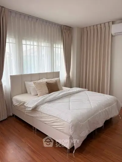 Cozy bedroom with elegant curtains and wooden flooring, featuring a comfortable bed and soft lighting.