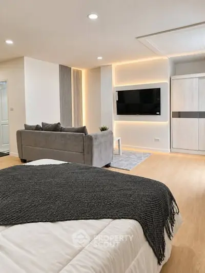 Modern bedroom with sleek TV setup and cozy sofa, featuring elegant lighting and wooden flooring.