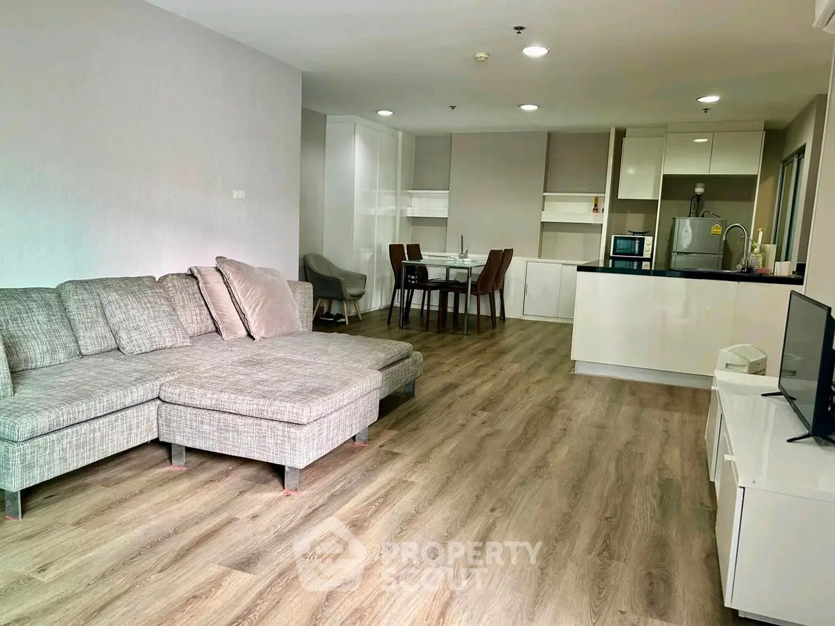 Spacious open-plan living room with modern kitchen and dining area, featuring stylish furniture and wood flooring.