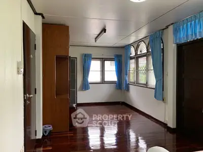 Spacious room with polished wooden floors and blue curtains, ideal for versatile living space.