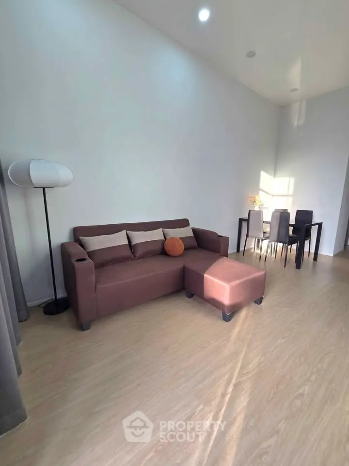 Modern living room with brown sofa and dining area, featuring elegant wooden flooring.