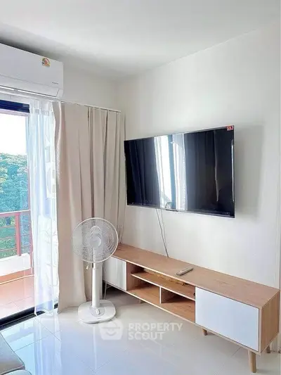 Modern living room with wall-mounted TV and balcony view, featuring sleek furniture and natural light.