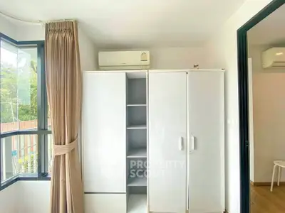 Bright bedroom with large window and white wardrobe, featuring air conditioning for comfort.